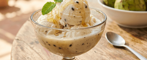 Creamy cherimoya ice cream with honey and mint in a glass bowl on wood.