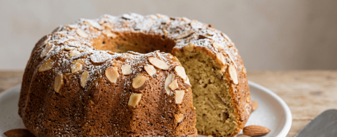 Bundt cake topped with sliced almonds and powdered sugar on a white plate with a cake slicer