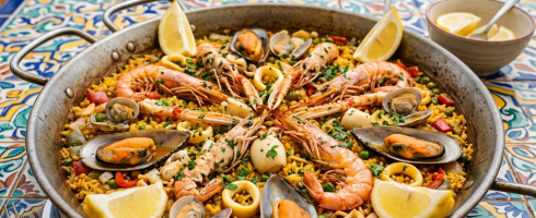 Seafood paella with shrimp, mussels, clams, squid, lemon wedges, and yellow rice on a decorative table with ocean view