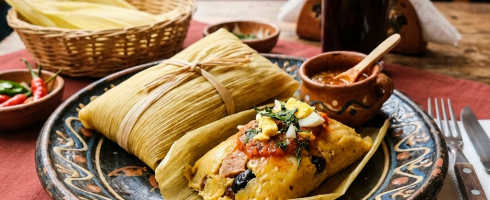 Traditional Guatemalan tamales wrapped in corn husks on a decorative plate with salsa and a drink