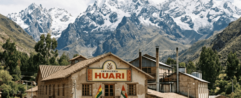 Cervecería Huari brewery building with Bolivian and regional flags and people outside, set against snow-covered mountain range.
