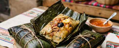Tamales wrapped in banana leaves on a plate with red salsa