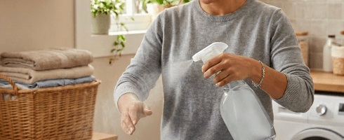 Woman ironing a blue button-up shirt while spraying wrinkle release spray
