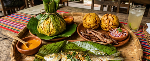 Traditional Belizean meal with fish, tamales, fried food, dipping sauce, and a drink