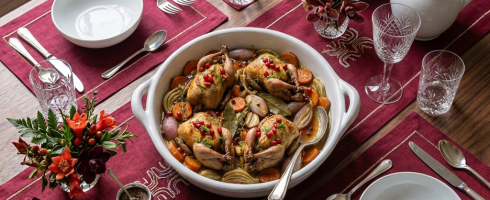 Four roasted birds in a clay dish with vegetables and pomegranate seeds